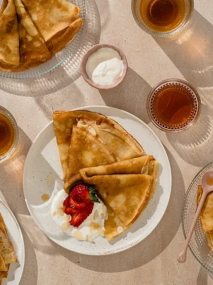 Crêpes fines dorées servies avec du miel, entourées de verres de thé