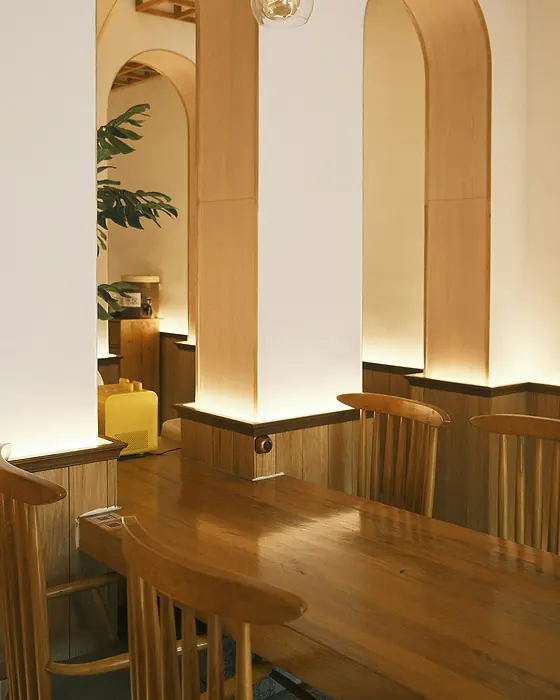 Salle de café baignée d’une lumière chaude, avec des niches en arc et un comptoir en bois